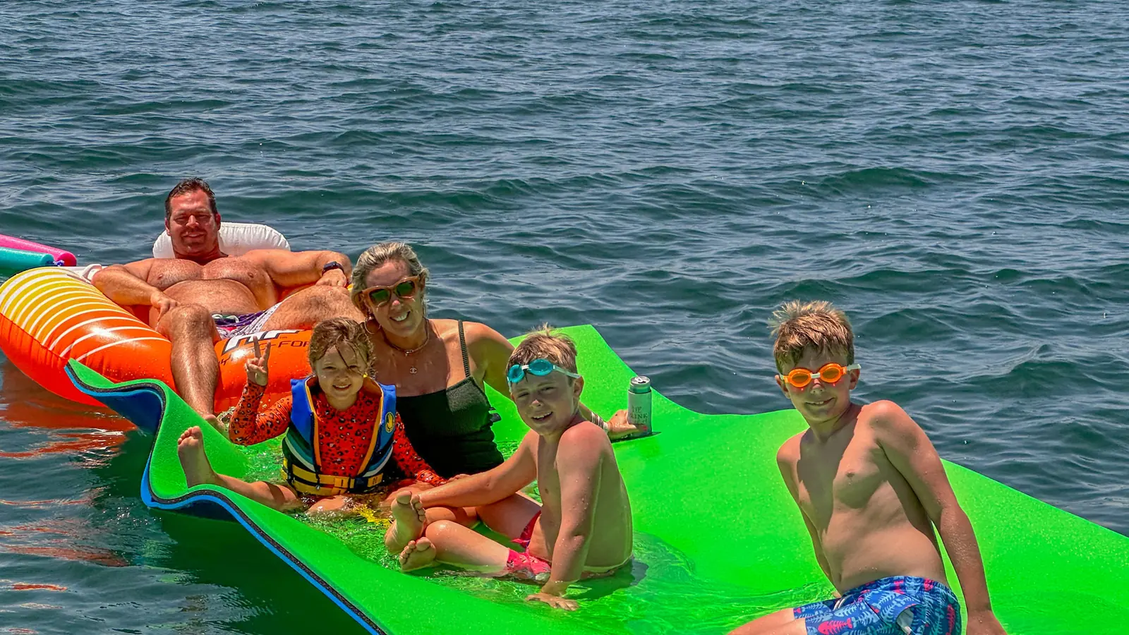 Family relaxing together on a floating mat beside a yacht