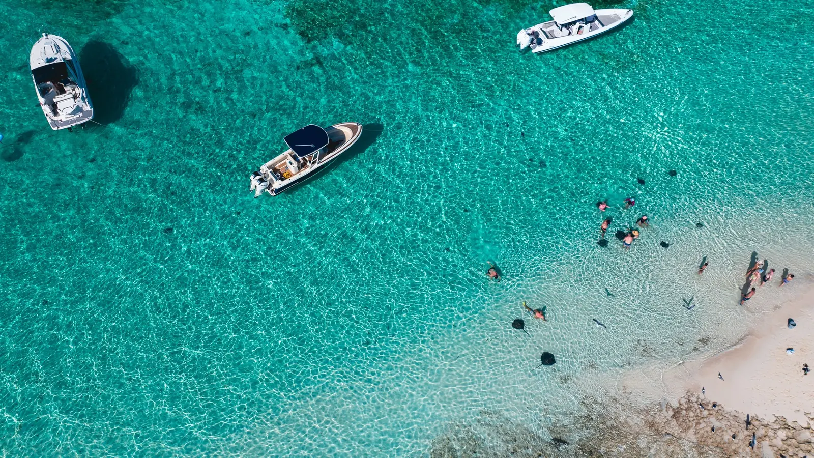 Swimmers beside boats in clear shallow water